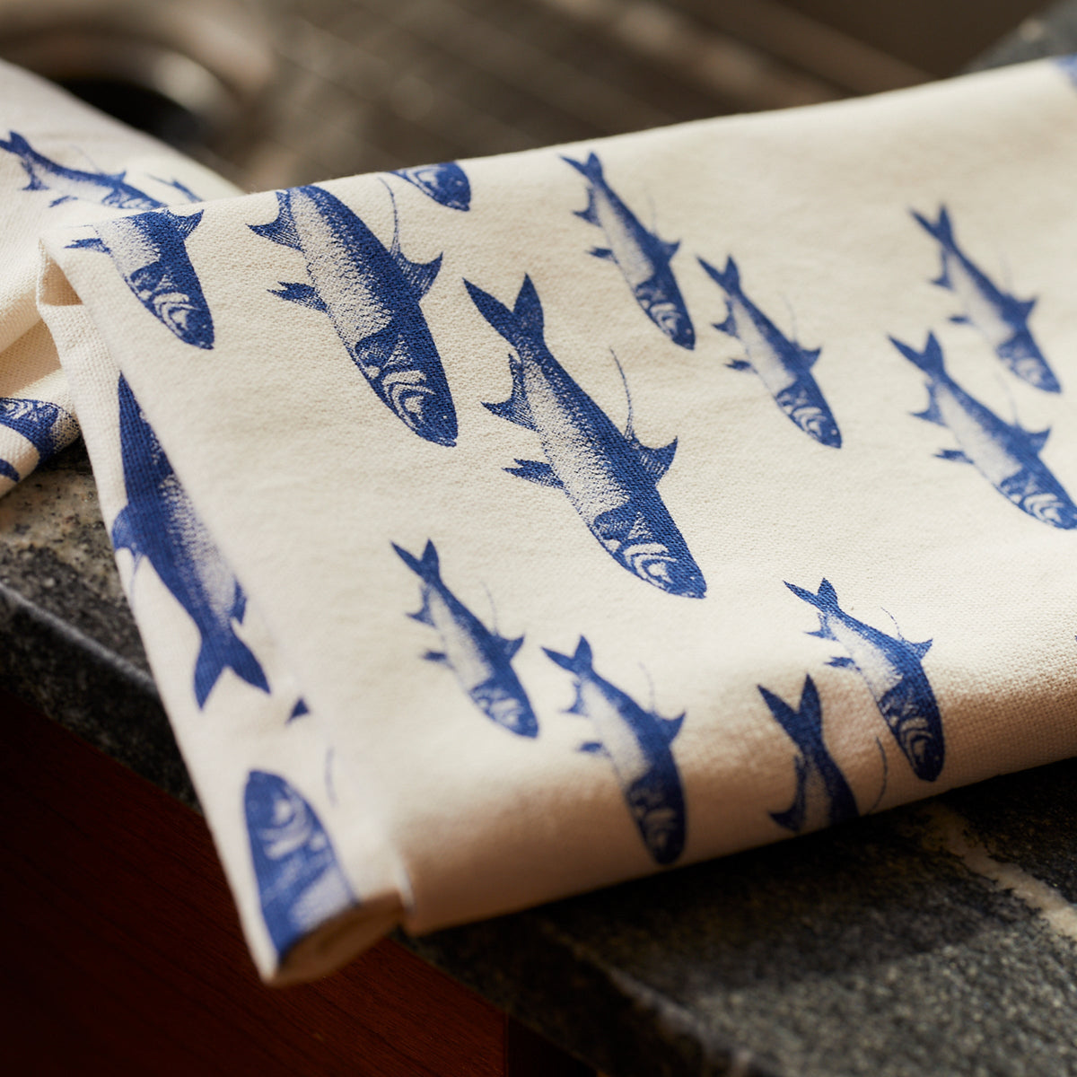 A blue and white School of Fish Kitchen Towel, Set of 2 from Caskata draped over a kitchen countertop.