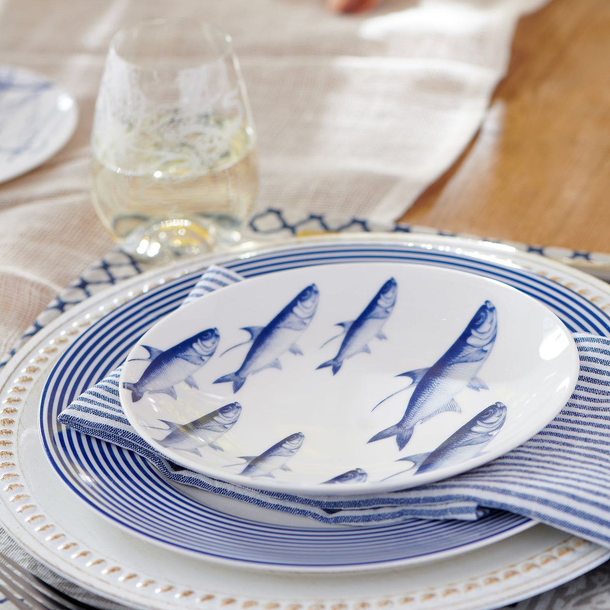 A Caskata Artisanal Home Newport Racing Stripe Rimmed Dinner Plate with fish on it.