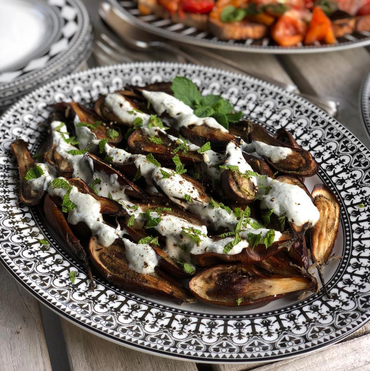 A decorative black and white Casablanca Oval Rimmed Platter from Caskata Artisanal Home with grilled eggplant drizzled with white sauce and garnished with chopped herbs.
