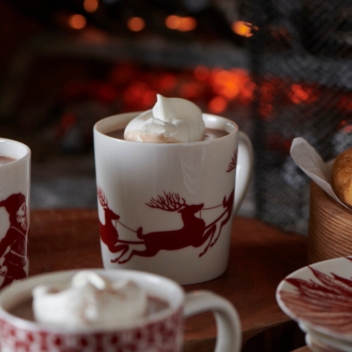 Three Holiday Mugs Mixed Sets of 12 of hot cocoa on a table next to a fireplace during the holiday season.