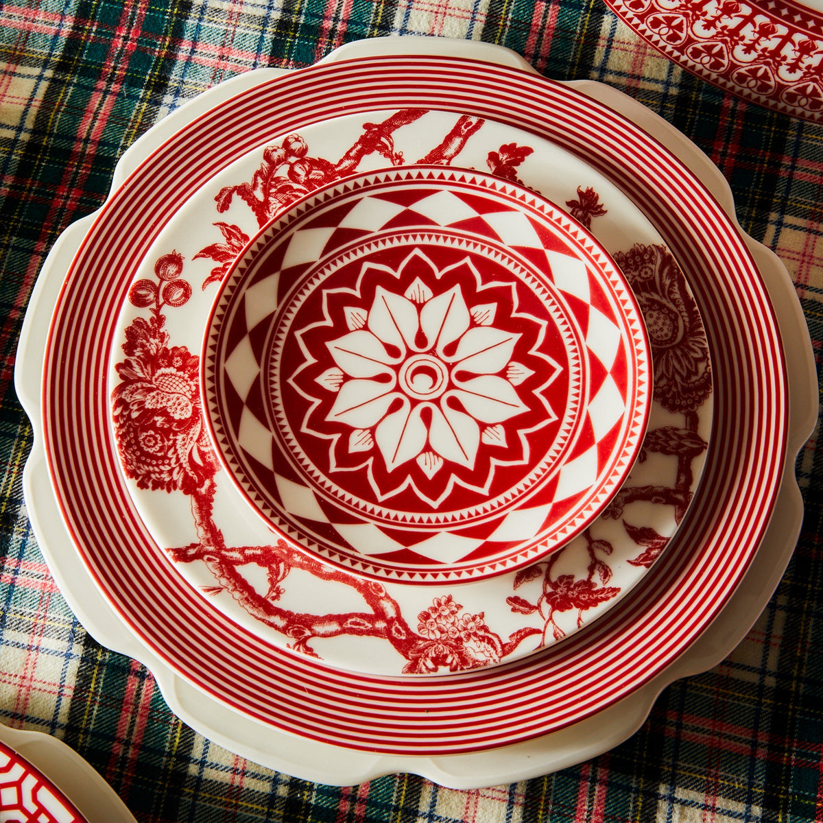 A set of three Fez Crimson Small Plates by Caskata Artisanal Home, an entertaining powerhouse, sits stacked on a table covered with a plaid tablecloth.