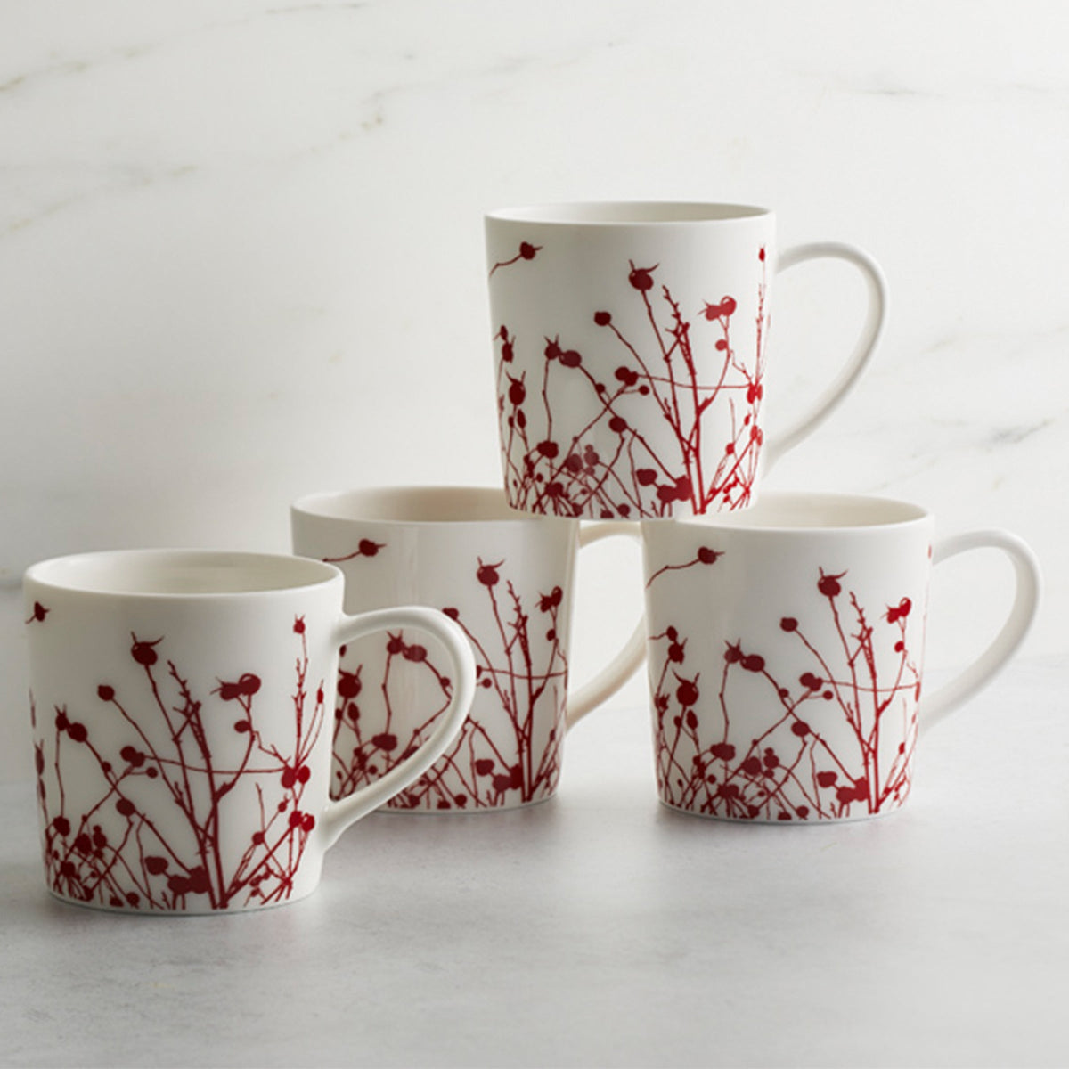 Four generously sized Winterberries Mugs made of creamy white porcelain, each adorned with a red floral pattern reminiscent of winter berries from Caskata Artisanal Home, are arranged on a white surface against a light background.