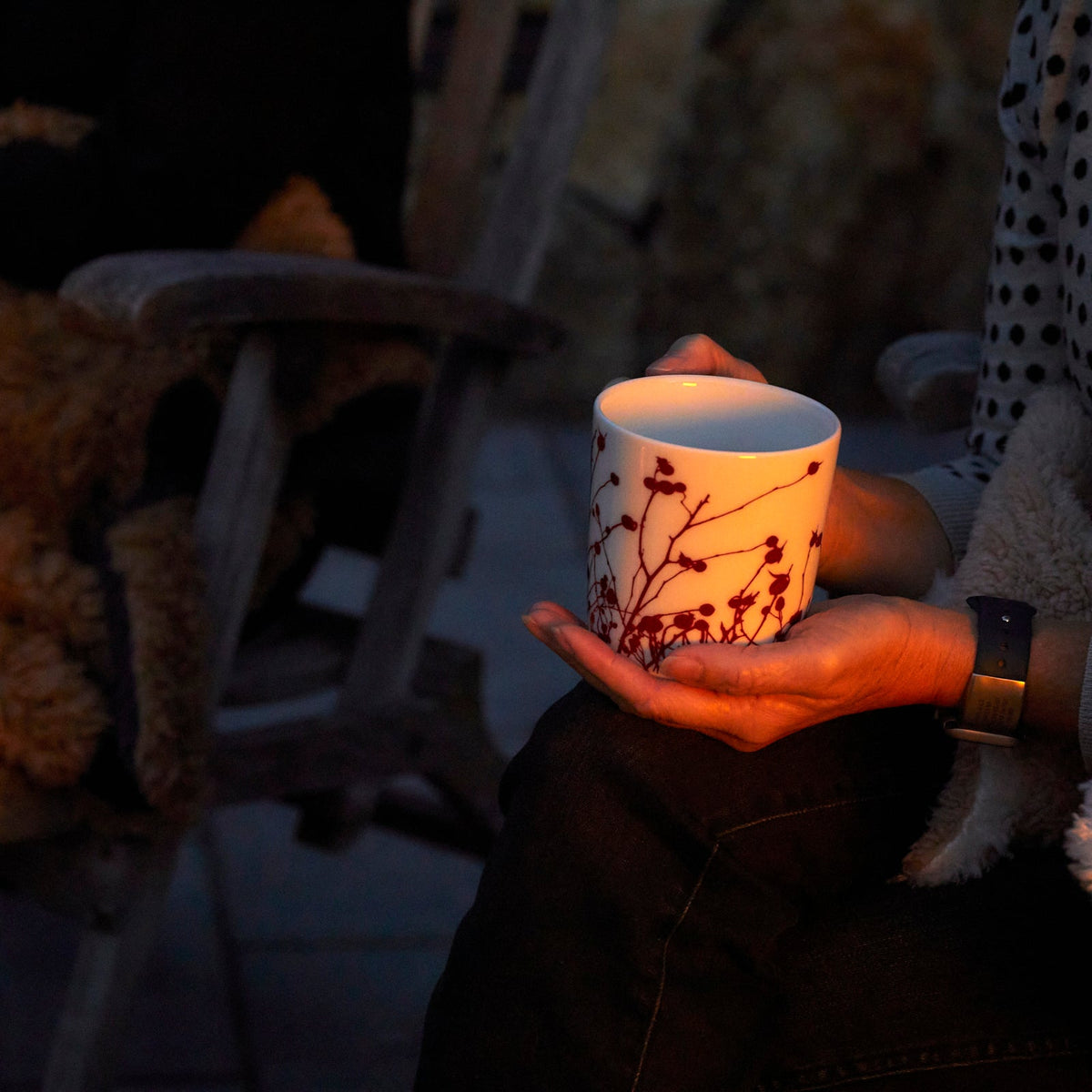 A person holding a generously sized Caskata Artisanal Home Winterberries Mug, sitting in a dimly lit setting.