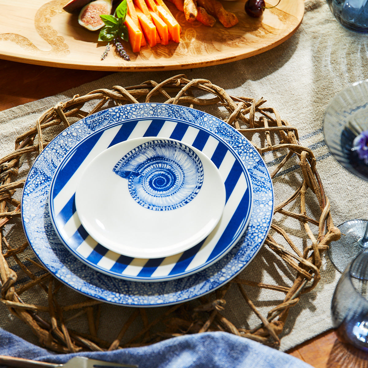 A blue and white coastal place setting featuring Sea Fan Dinner, Beach Towel Stripe Salad, and Shells Canapé by Caskata.