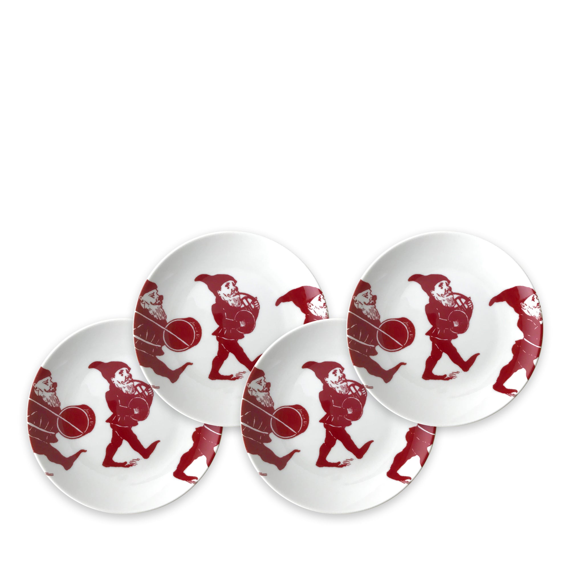 Four white plates, part of an heirloom-quality dinnerware holiday collection, each feature an illustration of a red gnome holding a drum. They are called Elves Small Plates by Caskata Artisanal Home.