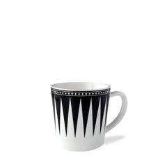 The Marrakech Mug by Caskata Artisanal Home is a white high-fired porcelain coffee mug with a black geometric triangular pattern and a black border adorned with small white stars near the rim, reminiscent of Art Deco designs.