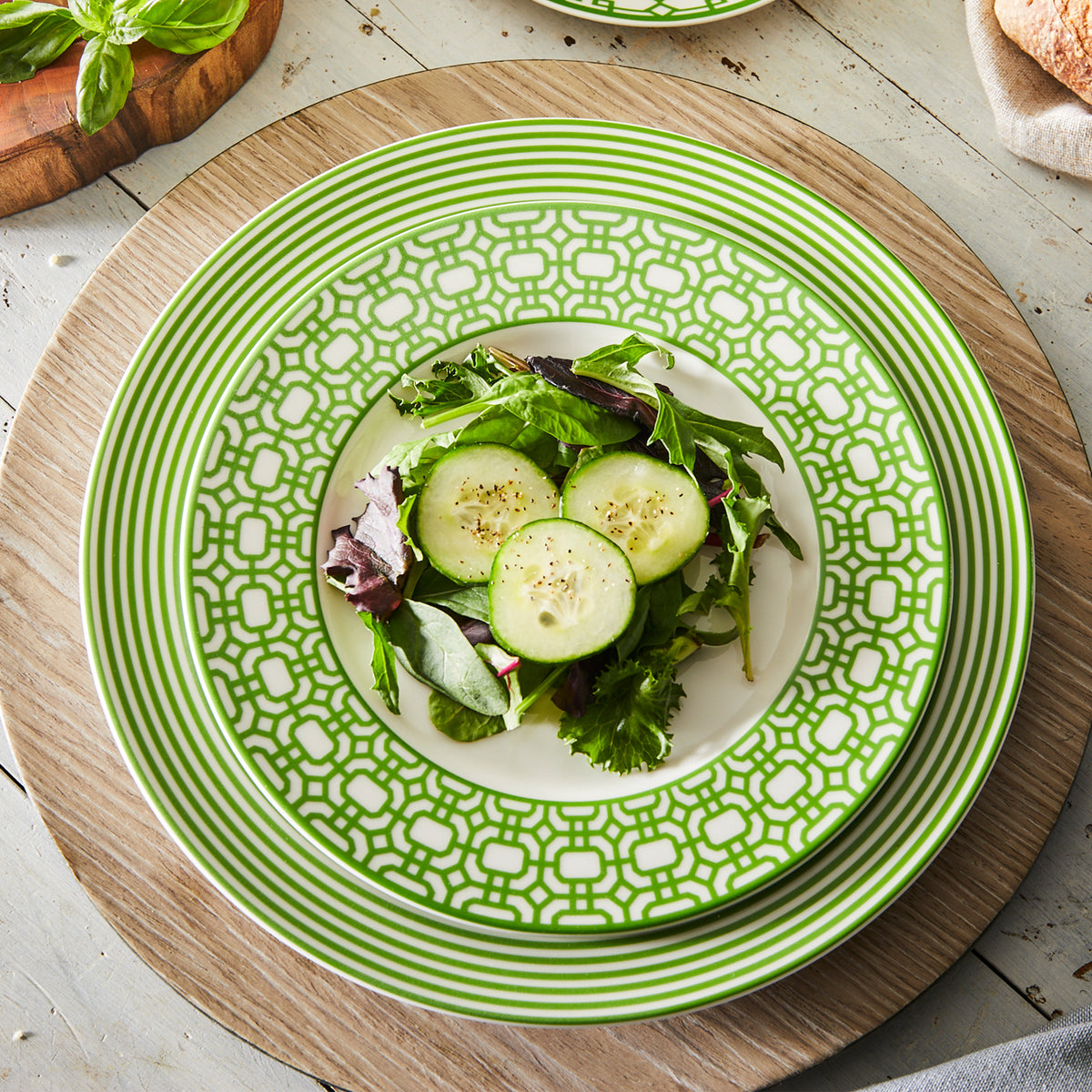 A salad with cucumber slices and mixed greens on a decorative Newport Stripe Verde Rimmed Dinner Plate, made of high-fired porcelain, placed on a wooden table setting by Caskata Artisanal Home.