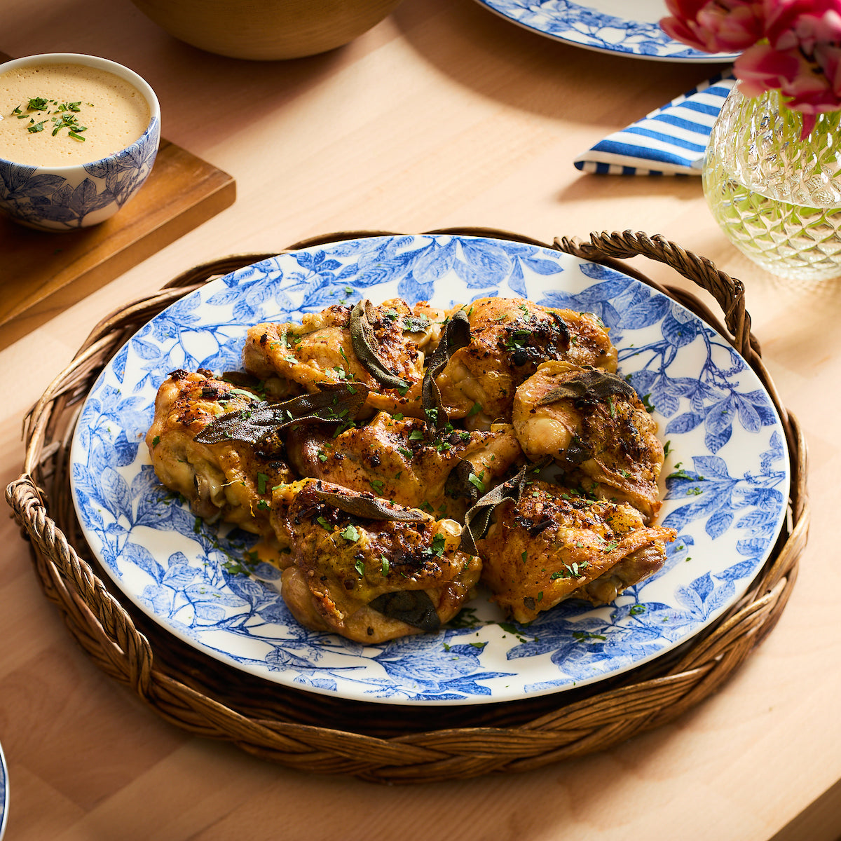 A Blue Arbor Charger Plate holds sage and chili oil roasted chicken thighs on a wood table.