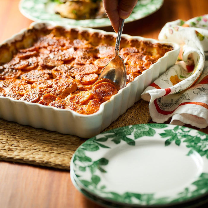 Someone is dipping a serving spoon into a baking dish full of sweet potato gratin.