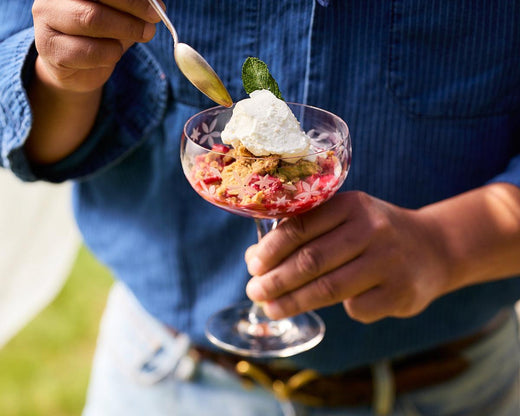 A man in a blue shirt holds a Chatham Bloom Coupe Glass with a serving of strawberry rhubarb crumble.