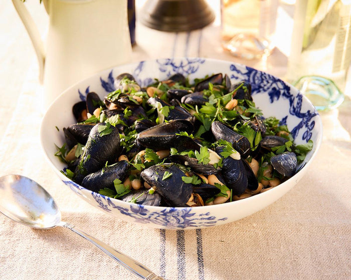 A blue and white porcelain Arcadia Serving Bowl full of cooked mussels.
