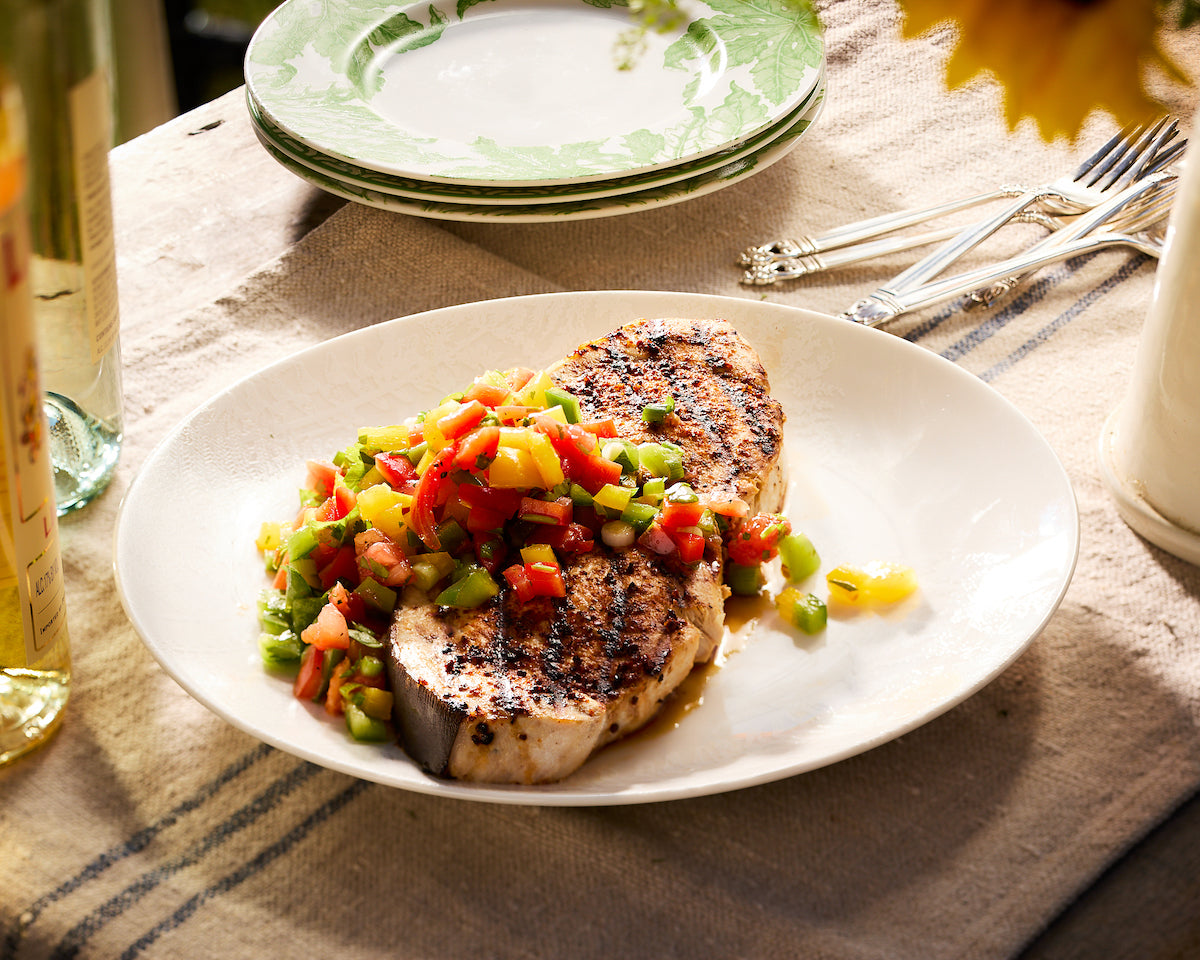A large grilled swordfish steak topped with diced red, yellow and green peppers.