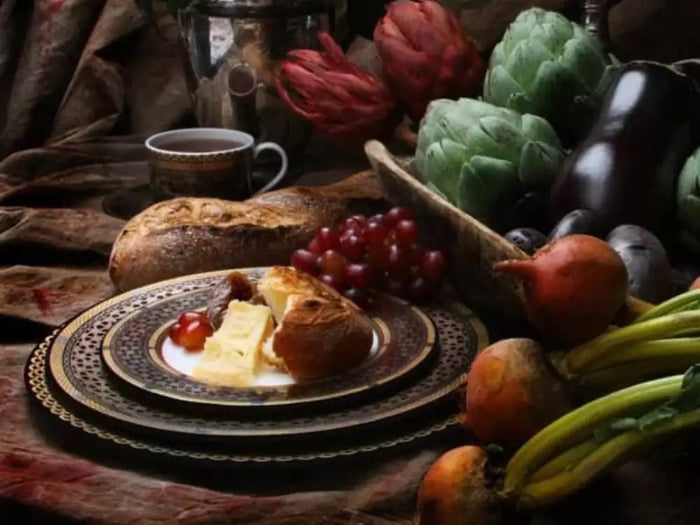 Hawthorne Onyx Gold & Platinum dinnerware by Caskata, layered with bread, cheese, grapes, and seasonal vegetables on a rustic table setting