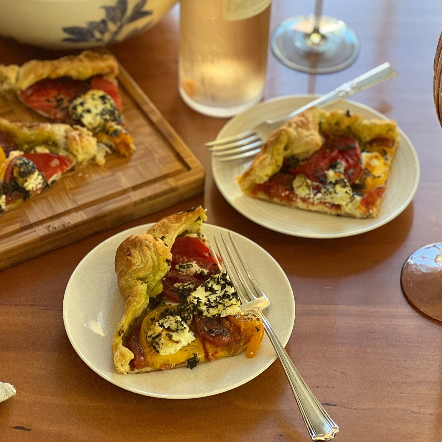 Two slices of tomato tart are on small plates with silver forks.