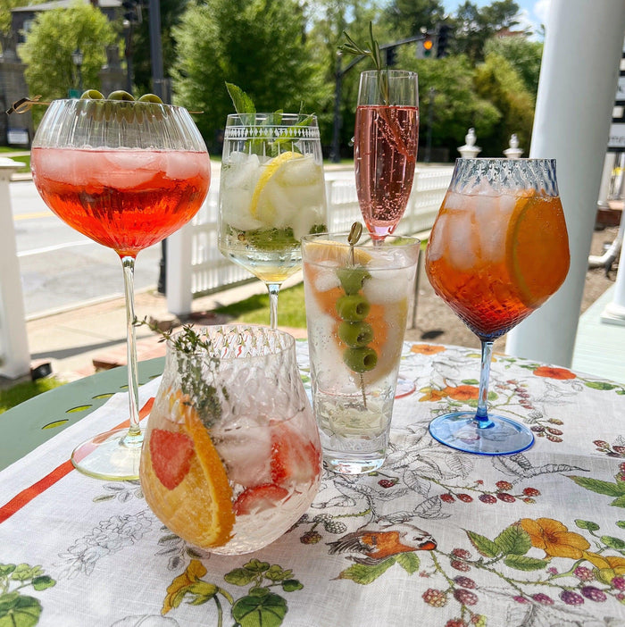 Six spritz cocktails in a variety of glasses on a table outside.