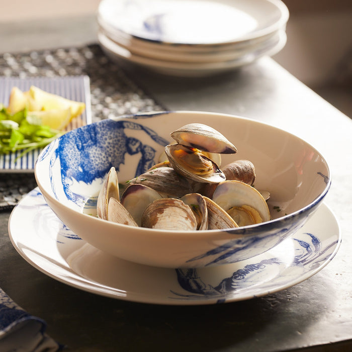 A wide porcelain coupe soup bowl adorned with blue crabs holds countneck clams steamed with garlic, white wine, butter and fresh herbs.