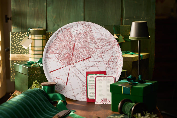 Holiday-themed Caskata platter featuring a vintage red map design, styled among green gift boxes, ribbon, and festive wrapping supplies for a Christmas gifting scene.
