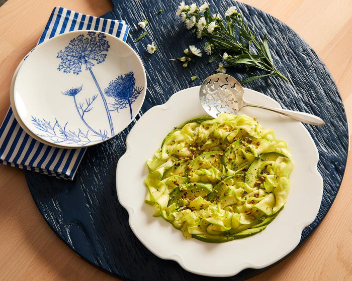 A blue serving board with a blue Summer Blues floral salad plate and a Grace white charger plate with zucchini carpaccio.