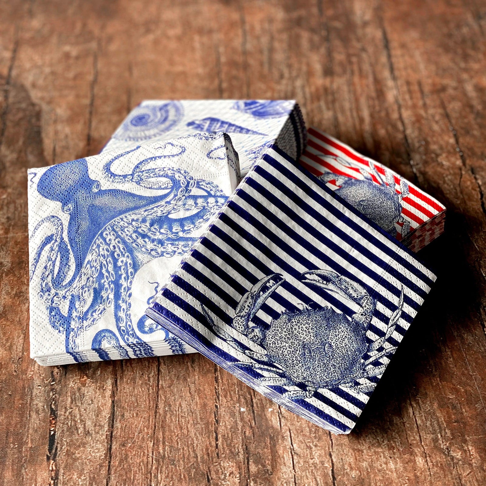 Three stacks of napkins with blue and red sea life designs, including an octopus, crab, and stripes, on a wooden surface.