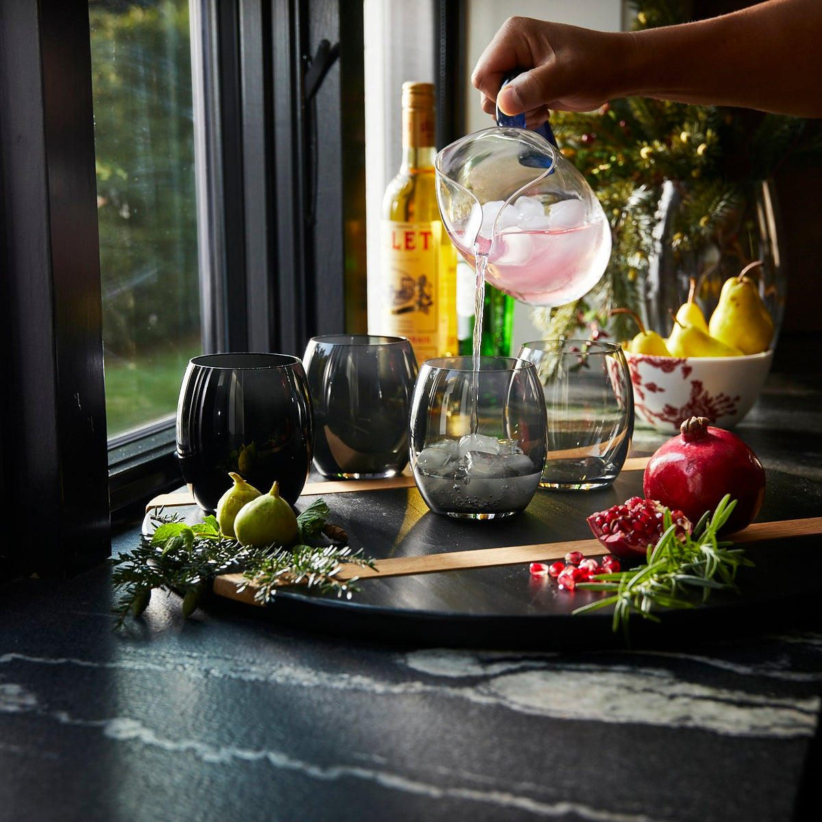 A person pouring a drink into a Les Nuages Gray Ombré Glasses Set of 4 by Caskata.