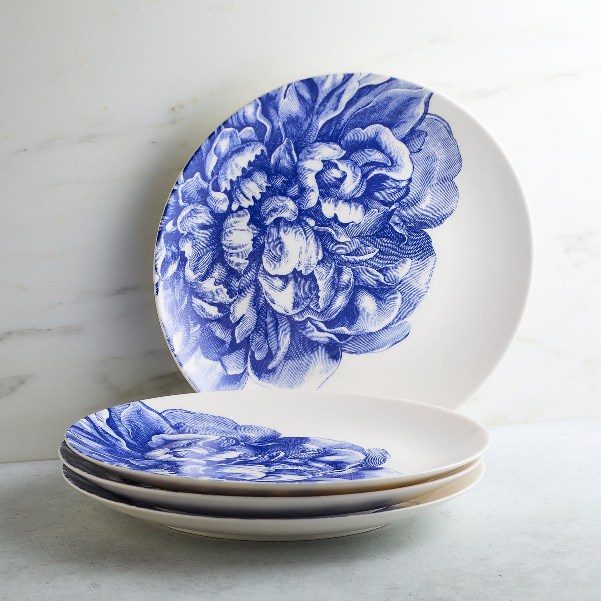 Two Peony Coupe Dinner Plates from Caskata Artisanal Home, one upright and one stacked, against a marble background.