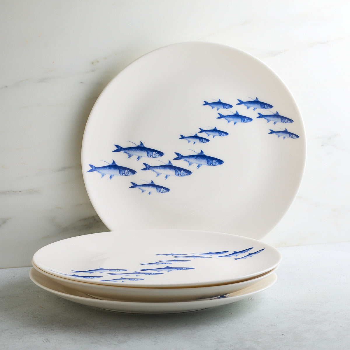 Two white Caskata Artisanal Home School of Fish Coupe Dinner Plates stacked against a marble background.