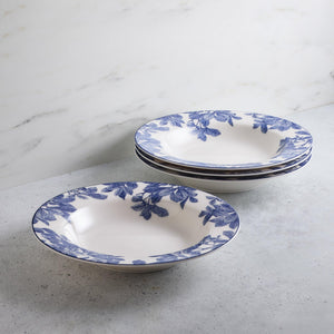 A set of four white high-fire porcelain bowls with blue floral patterns. Three Arbor Rimmed Soup Bowls from Caskata Artisanal Home are stacked while one lies next to the stack on a gray countertop with a white marble background.