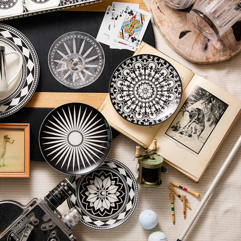 Aerial view of heirloom-quality, Caskata Artisanal Home Casablanca Small Plates, playing cards, a camera, an open book, colored pencils, glassware, and a golf ball arranged on a table.