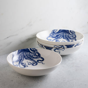 Four premium Lucy Entrée Bowls by Caskata Artisanal Home, each adorned with blue octopus designs, are stacked on a gray surface against a white marble background, evoking a sense of deep-water whimsy.