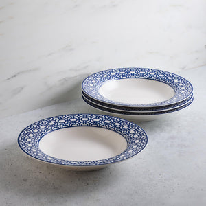A stack of premium Newport Garden Gate Rimmed Soup Bowls from Caskata Artisanal Home, with a blue geometric pattern around the rim, placed on a gray surface against a white marble background. This dinnerware adds elegance to any contemporary tableware collection.