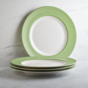 A stack of Caskata Artisanal Home Newport Stripe Verde Rimmed Dinner Plates, with one plate standing vertically against a marble backdrop.