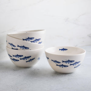 A stack of four Caskata School of Fish Cereal Bowls, each decorated with a pattern of blue fish, makes a charming addition to any dinnerware collection.
