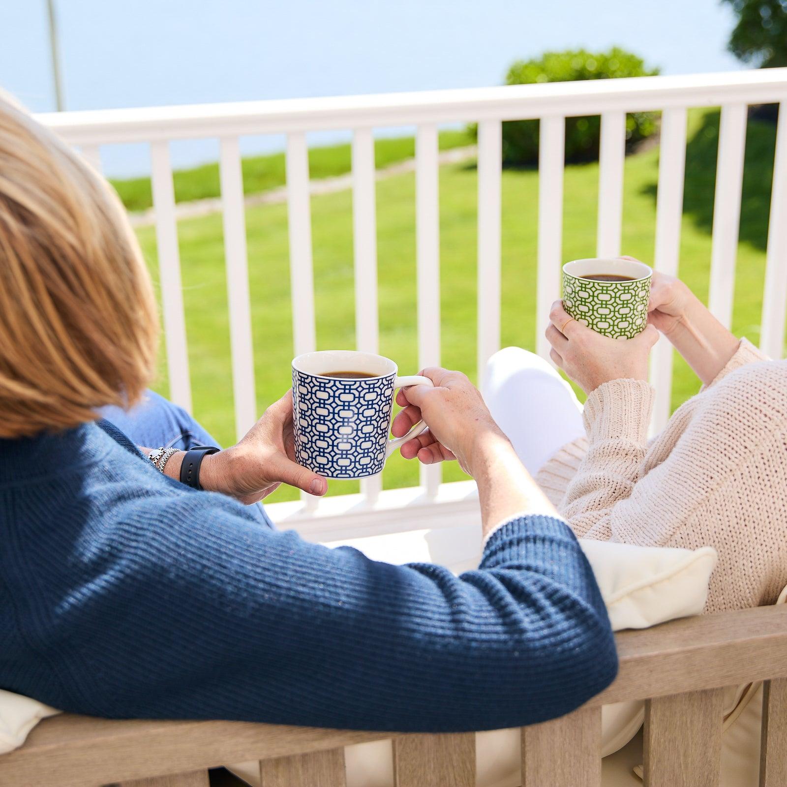 A creamy white Newport Garden Gate Mug by Caskata Artisanal Home, delicately adorned with a blue geometric pattern, features a handle on the right side. This graphic mug is both dishwasher and microwave safe, ensuring convenience and style in your daily routine.