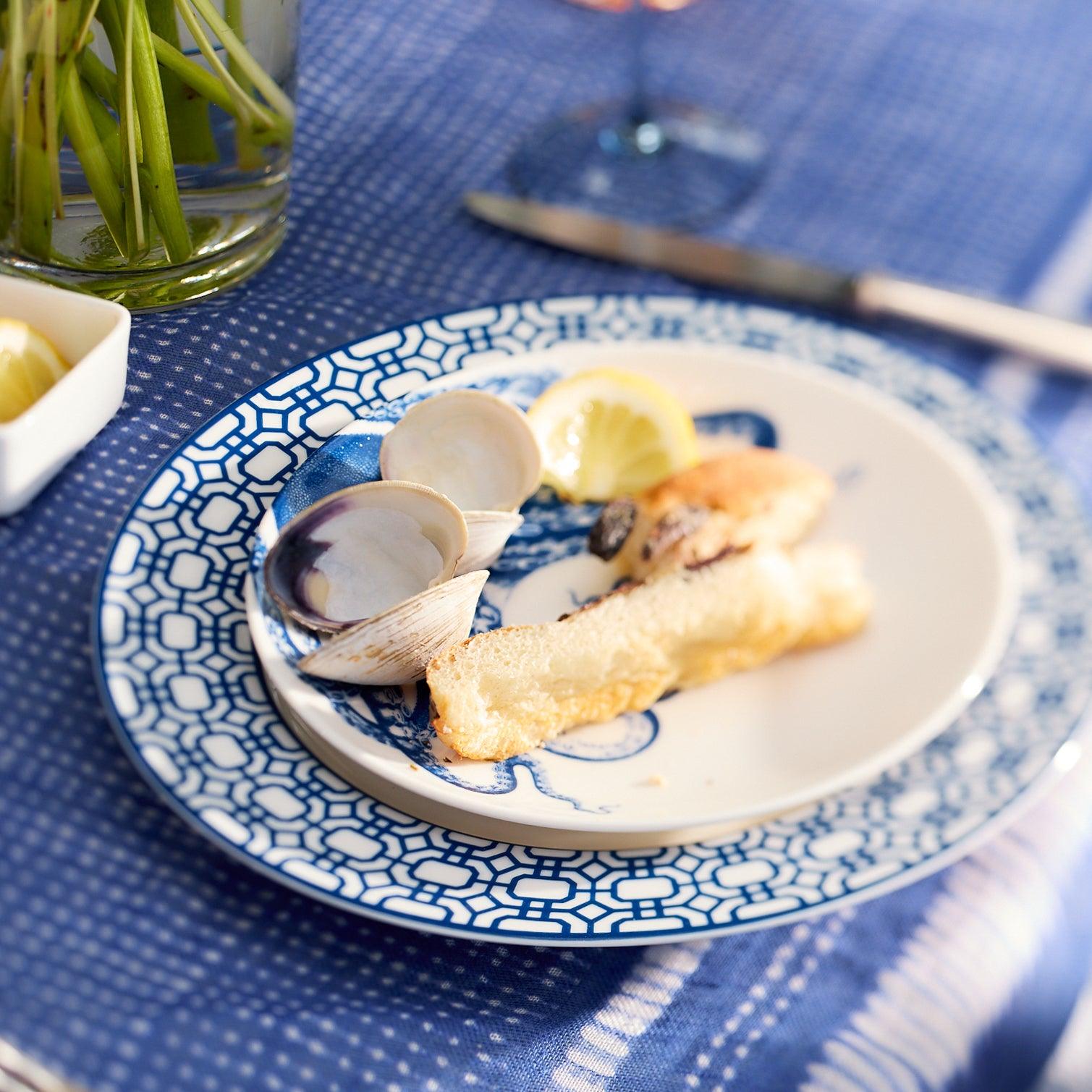A Newport Garden Gate Rimmed Salad Plate with a blue geometric pattern around the rim, crafted from premium porcelain by Caskata Artisanal Home, perfect for adding a touch of elegance to any table setting.