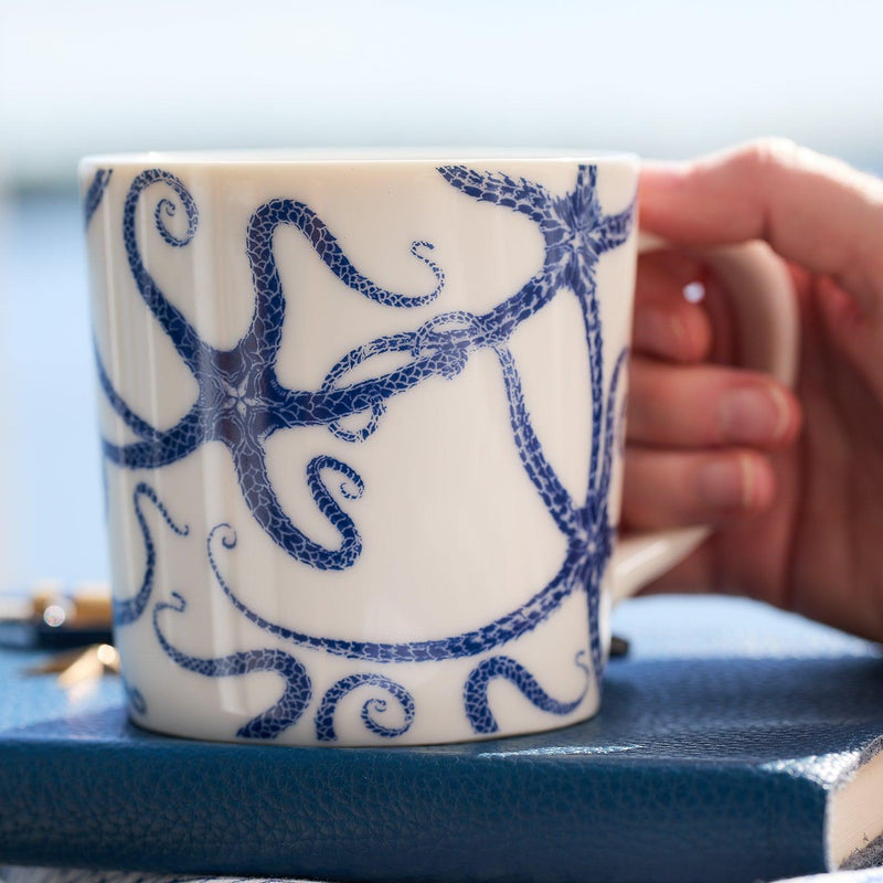 A hand holds a high-fired porcelain Starfish Mug from Caskata Artisanal Home, resting on a blue notebook.