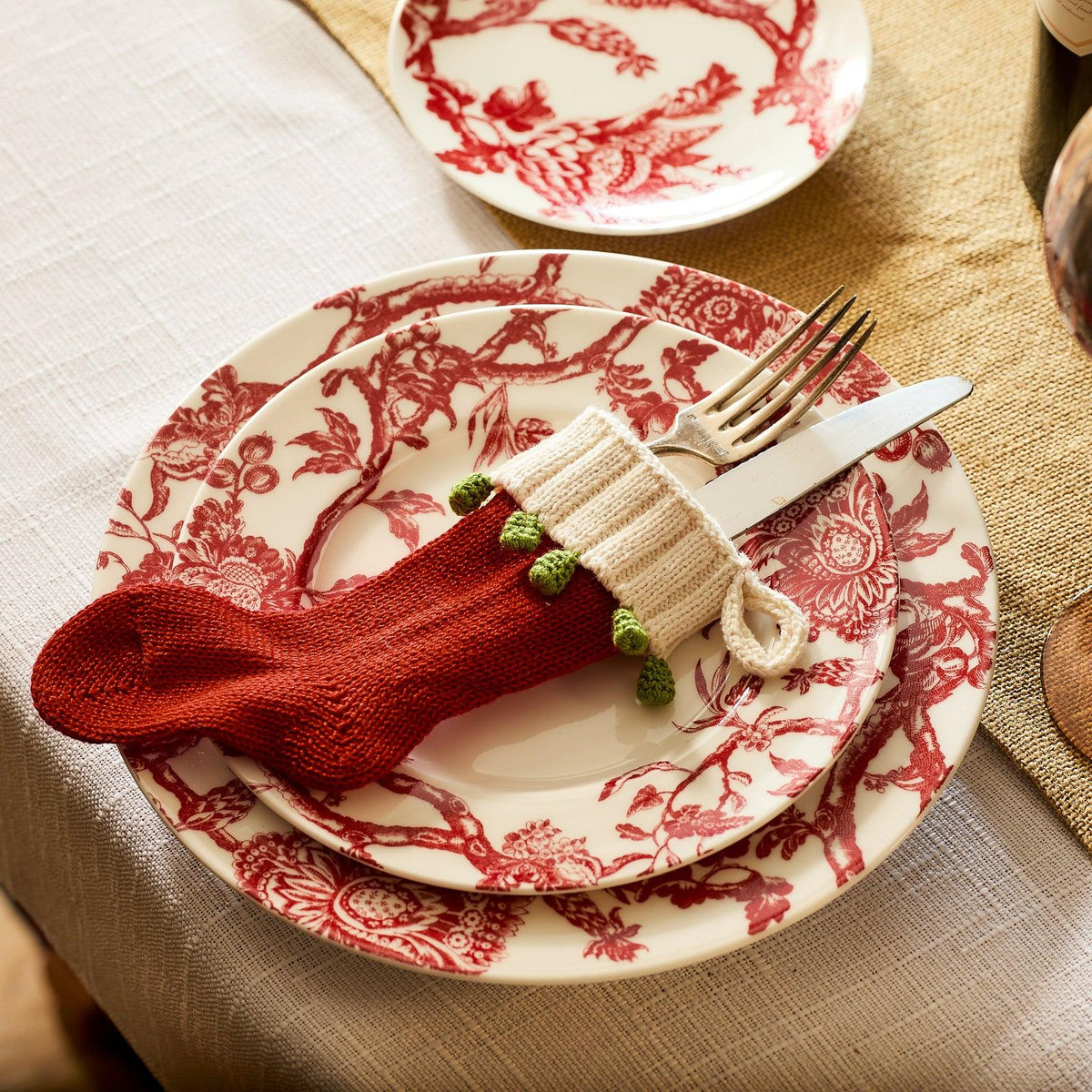 A set of Arcadia Crimson Rimmed Salad Plates from Caskata Artisanal Home, with silverware wrapped in a small red Christmas stocking placed on the top plate.