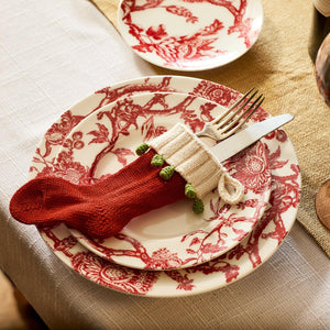 A set of Arcadia Crimson Rimmed Salad Plates from Caskata Artisanal Home, with silverware wrapped in a small red Christmas stocking placed on the top plate.