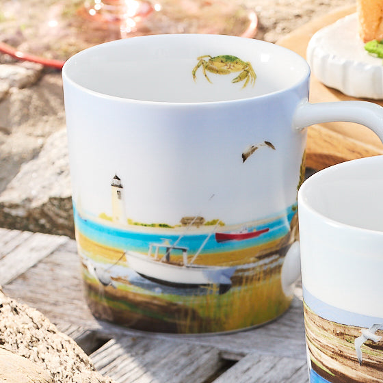 The Caskata X Felix Doolittle By the Sea Mug set features four white ceramic mugs beautifully illustrated with delicate watercolor scenes of a lighthouse, boats, and a flying bird, reminiscent of Felix Doolittle’s artwork. Each mug includes the charming detail of a small crab near the top for added character.