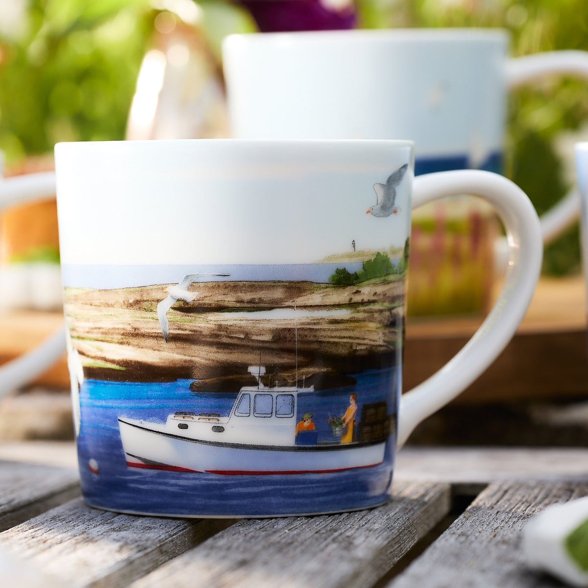 A Caskata X Felix Doolittle By the Sea mug, part of a set of 4, showcases a painted scene of a fishing boat on blue water with seagulls and a lighthouse in the background, elegantly placed on a wooden surface.