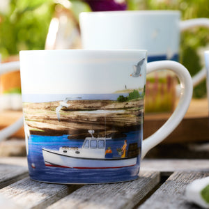 A Caskata X Felix Doolittle By the Sea mug, part of a set of 4, showcases a painted scene of a fishing boat on blue water with seagulls and a lighthouse in the background, elegantly placed on a wooden surface.