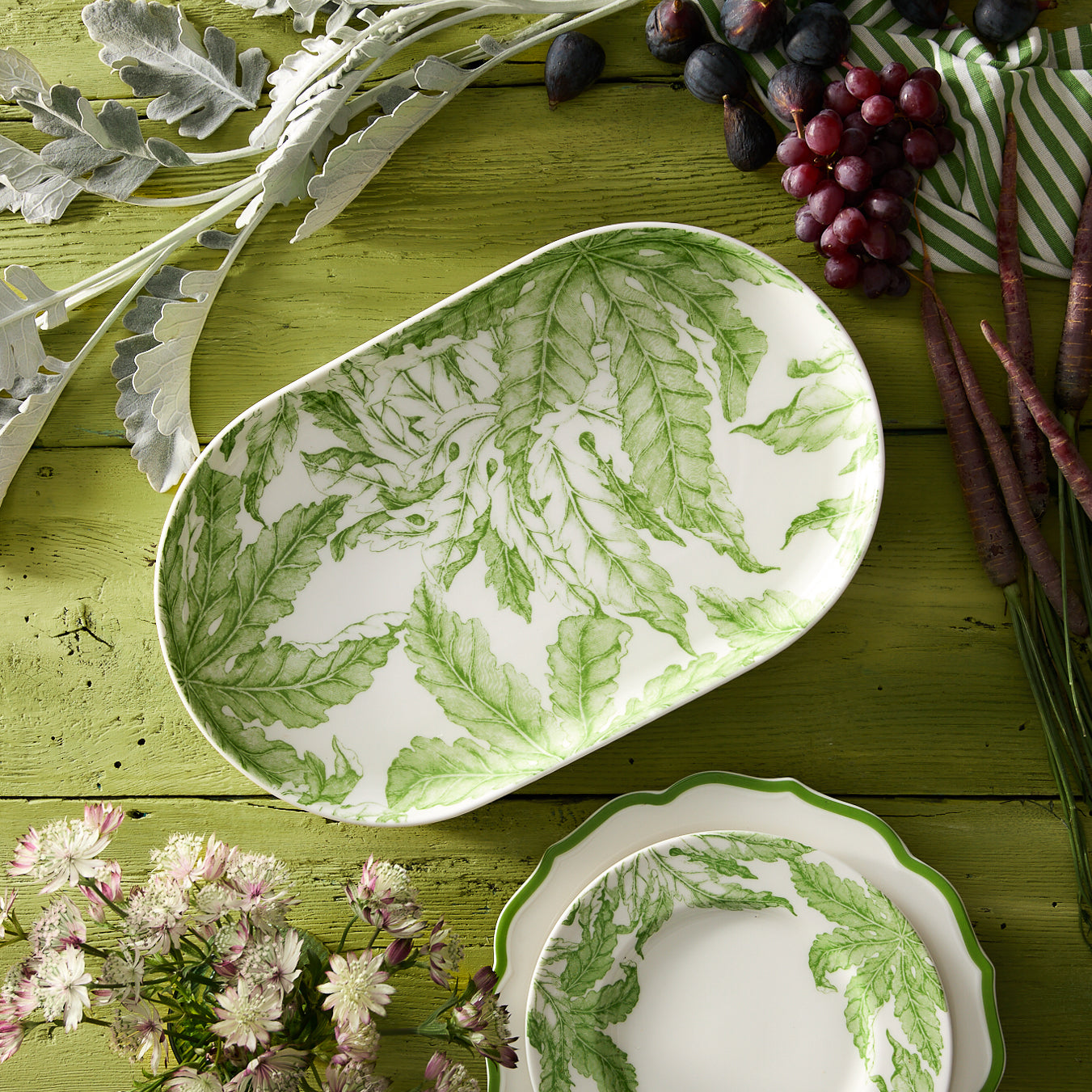 The Freya Large Coupe Oval Platter by Caskata features a stunning green botanical leaf pattern on a white porcelain background, making it an essential piece for entertaining.