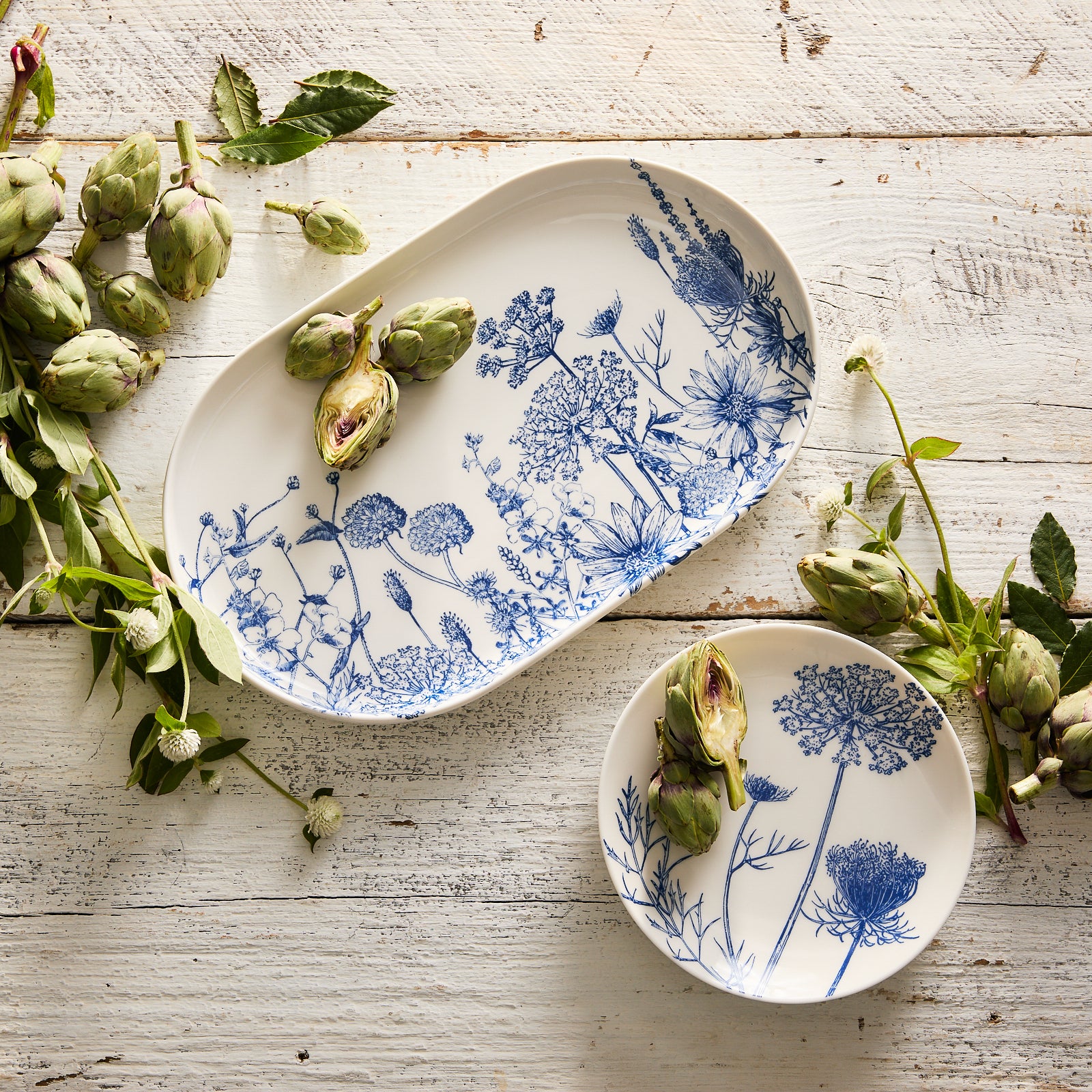 The Summer Blues Large Coupe Oval Platter by Caskata showcases exquisite blue floral illustrations on a white background and is crafted from high-fired porcelain.