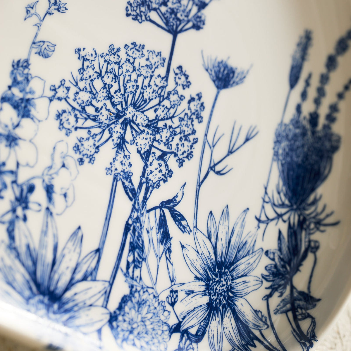 Featuring high-fired porcelain with intricate blue floral designs, the Caskata Summer Blues Large Coupe Oval Platter beautifully depicts various flowers and plants.