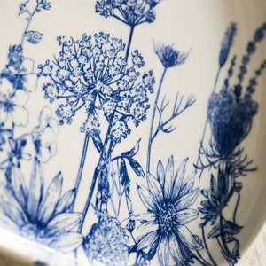 Featuring high-fired porcelain with intricate blue floral designs, the Caskata Summer Blues Large Coupe Oval Platter beautifully depicts various flowers and plants.