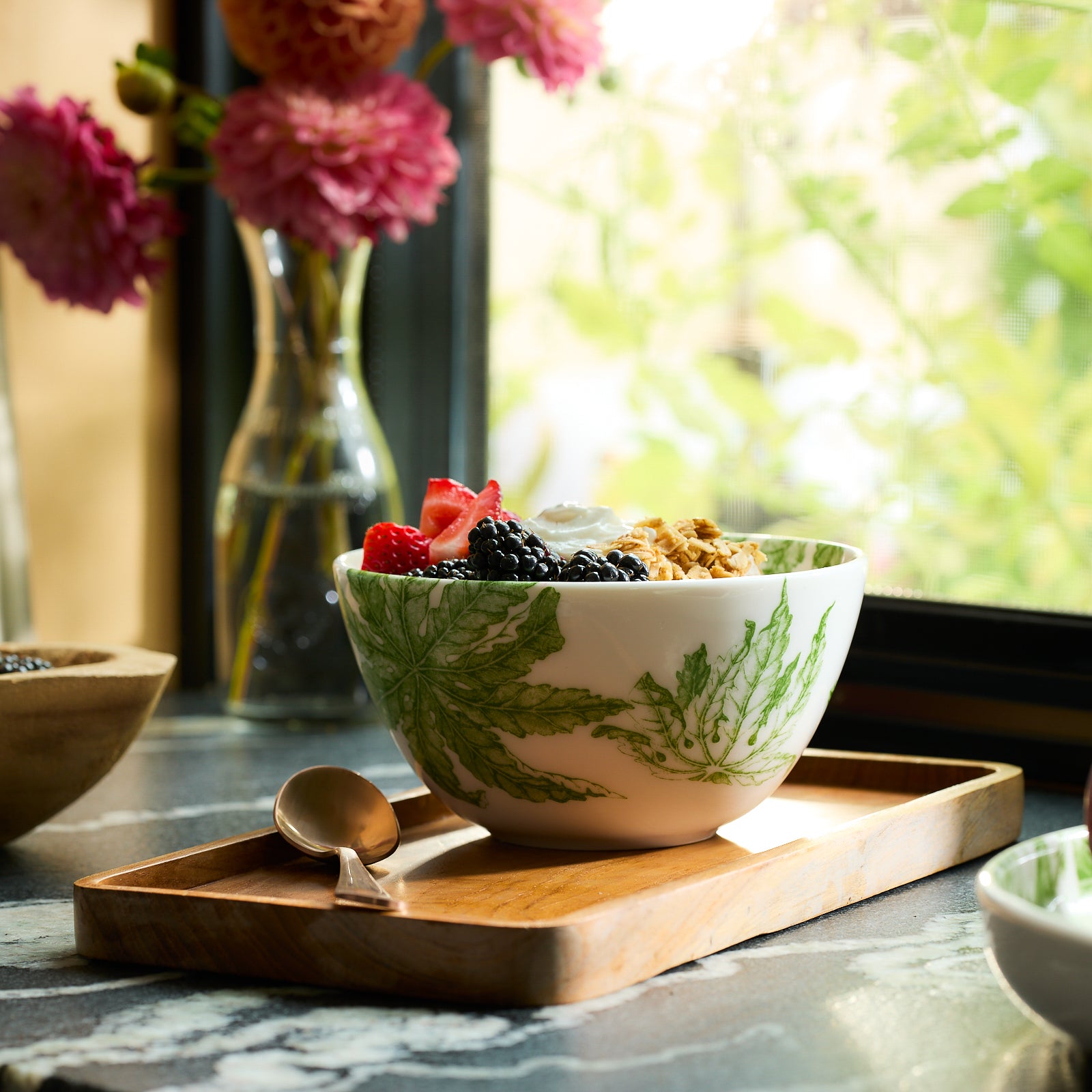 This Freya cereal bowl by Caskata, crafted from white porcelain and adorned with green leaf patterns, offers a blend of elegance and practicality as it is both dishwasher and microwave safe.