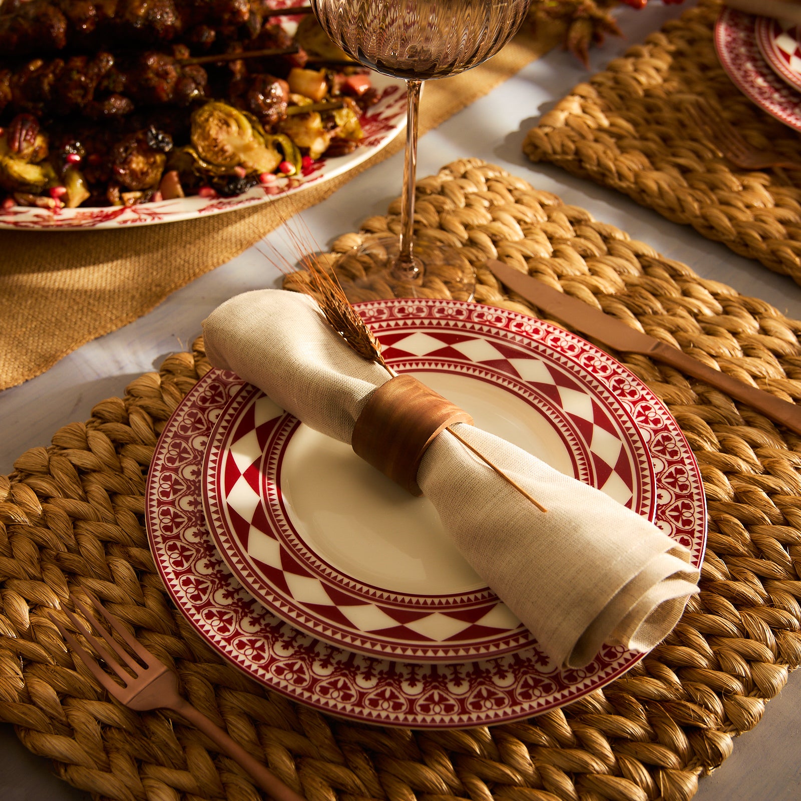 A Fez Crimson Rimmed Salad Plate from Caskata Artisanal Home, crafted from high-fired porcelain, features a white ceramic base adorned with a striking red and white geometric border inspired by Moroccan patterns of diamonds and triangles.