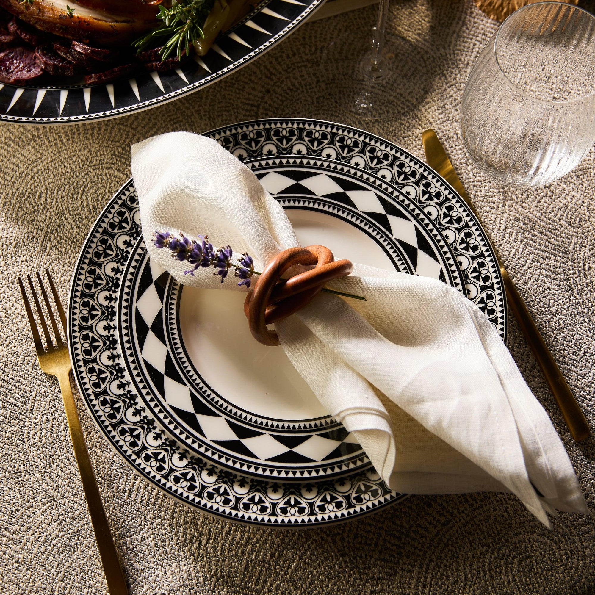 A Casablanca Rimmed Dinner Plate from Caskata Artisanal Home, featuring an intricate black floral pattern around the rim and hand-decorated details.