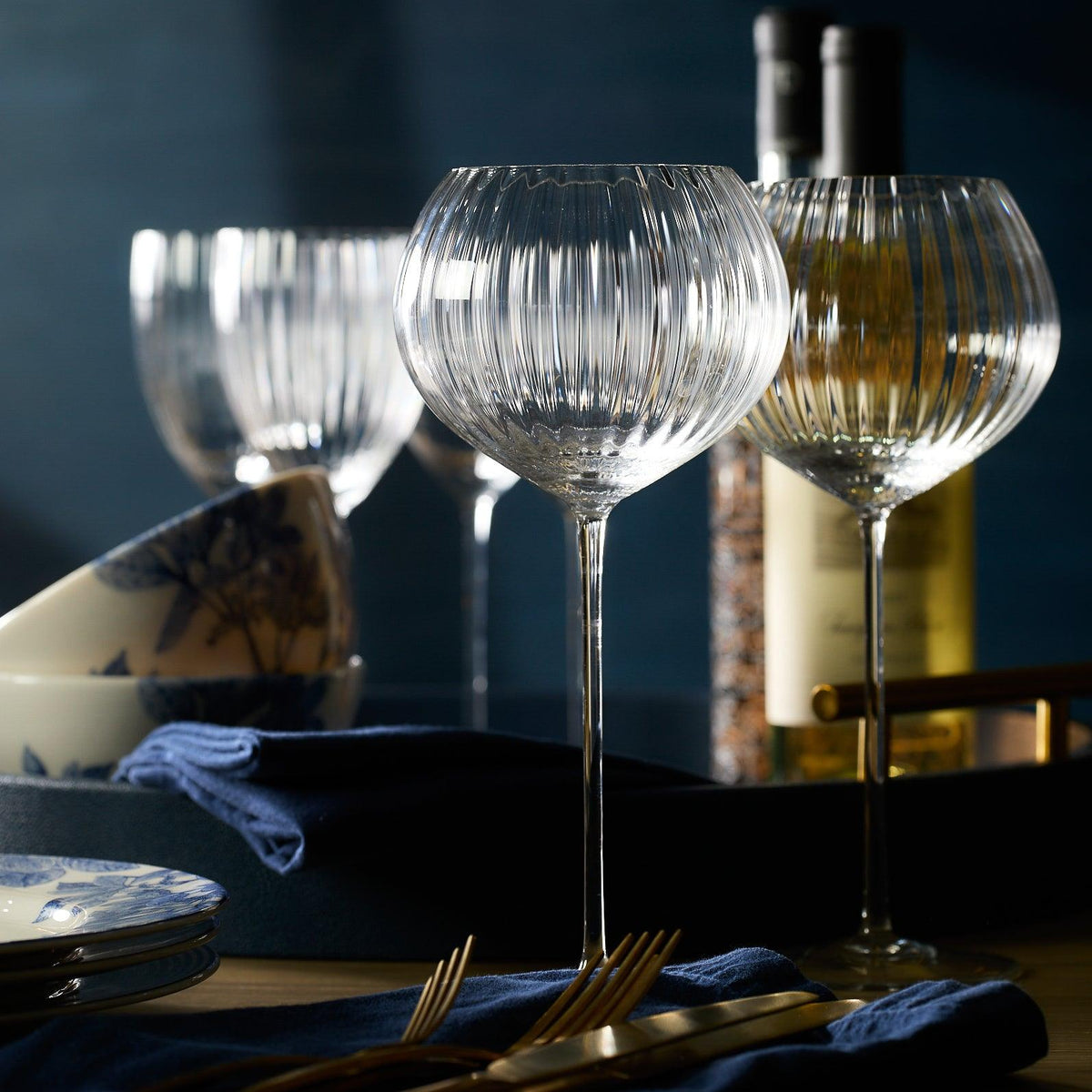 Quinn Clear Red Wine Glasses from Caskata Artisanal Home rest elegantly on the table, surrounded by folded napkins, plates, and a bottle in the background.