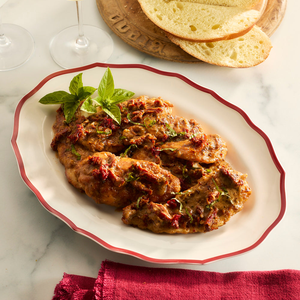 A Caskata Stella Crimson scalloped platter holds chicken cooked in a sauce with sun-dried tomatoes and topped with fresh basil.