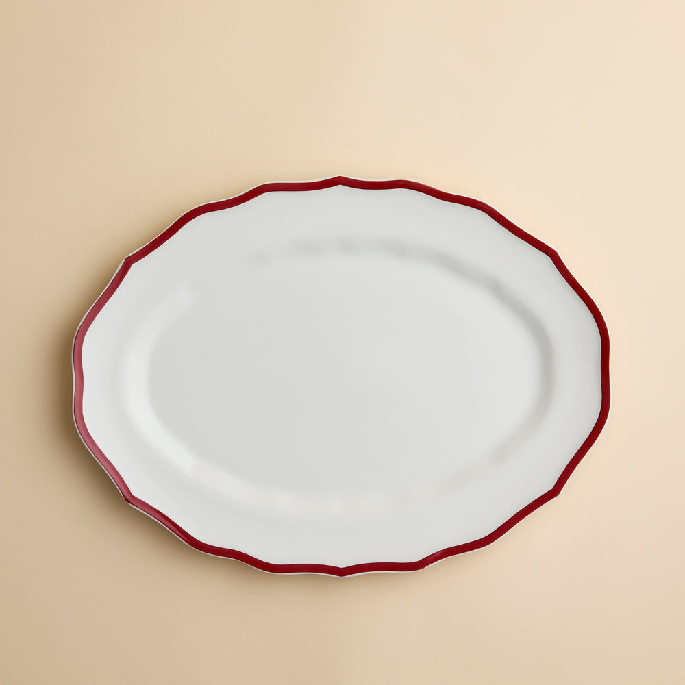 Caskata Stella Crimson Scalloped Platter in white porcelain with an oval shape and a thin red rim.